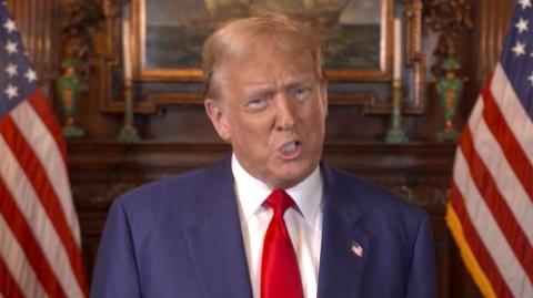 Donald Trump, flanked by US flags