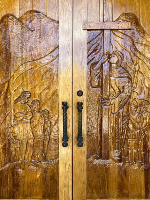 A carved church door at St. Peter's Catholic Church in Springerville, Arizona, depicts a Franciscan friar holding a cross in front of Native Americans on one side and Spanish conquistadors on the other.
