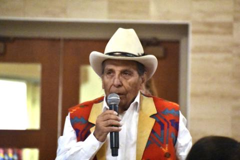 Donovan Archambault, 85. Former Chairman of Fort Belknap Indian Reservation Reservation, Montana, and Native American boarding school survivor, 2023. Archambault, wearing patterned vest and cowboy hat, speaks into microphone.