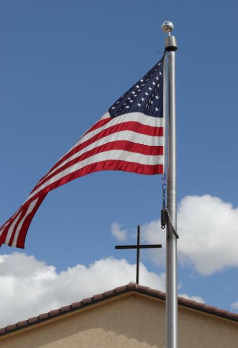 An American flag frames a cross atop a church.