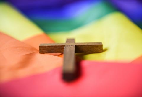 A wooden cross lies on a rainbow flag in this 2021 file photo. In an email to community members at the News Orleans Archdiocese school from which he was dismissed, Mark Richards said that he was fired because a parent notified officials about an obituary for his husband, who died in September 2023. (OSV News/KNA/Julia Steinbrecht)
