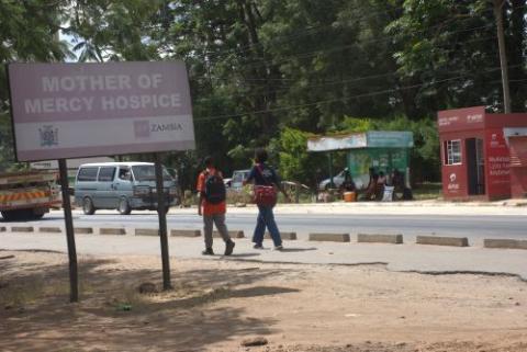 People walk on road near a sign for hospice. 