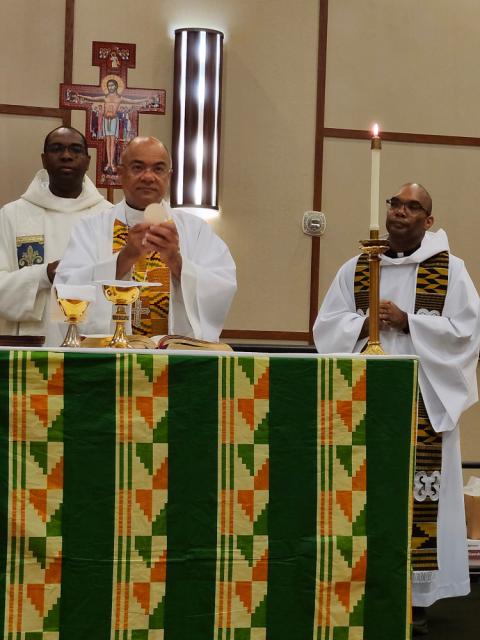 A dark green altar cloth with orange, yellow and lighter green stripes and geometric designs, designed and created by Sr. Jannette Pruitt, mid-Mass.