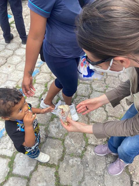 Sister Dondé offers a meal to a migrant child being held by his mother's hand. 