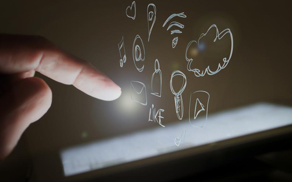 A photo illustration show a hand hovering over a smart device, with drawings of social media buttons and tags floating above the screen. (Pixabay/Edar)
