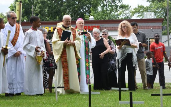 Fr. Victor Clore and members of Christ the King Parish in Detroit pause for a moment of silence July 22, 2017, in front of 44 crosses on the parish's front lawn, one for each of the lives lost in the city's violence of 1967. (CNS/The Michigan Catholic)