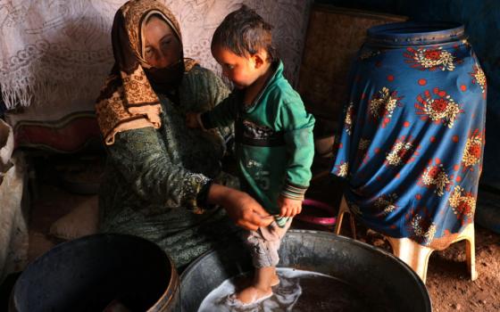 Fawza Umri helps her son put on clothes after being bathed inside their tent at Atmeh refugee camp, near the Turkish border in Syria, on June 13. (CNS/Reuters/Khalil Ashawi)