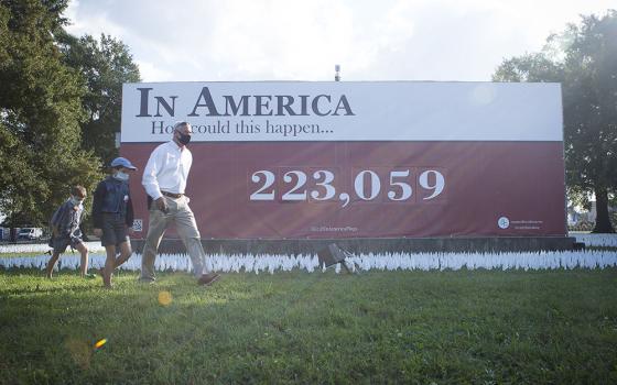 People in Washington walk near a temporary memorial for the victims of COVID-19 Oct. 23. Each day the artist adds new flags and changes the numbers to the installation as the death toll rises. As of Nov. 17, over 246,800 Americans had died from the diseas