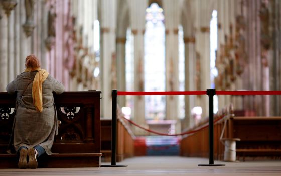 A woman prays alongside a barrier inside the Cologne Cathedral in Germany March 15, 2020, during the COVID-19 pandemic. (CNS/Reuters/Thilo Schmuelgen)