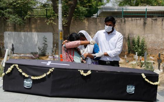 Relatives of a person who died after contracting COVID-19 mourn April 29 over the casket before the burial at a graveyard in New Delhi. (CNS/Reuters/Adnan Abidi)