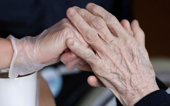 An employee holds the hand of a person at an elderly residence in Brussels April 14, 2020, during the COVID-19 pandemic. (CNS/Reuters/Yves Herman)