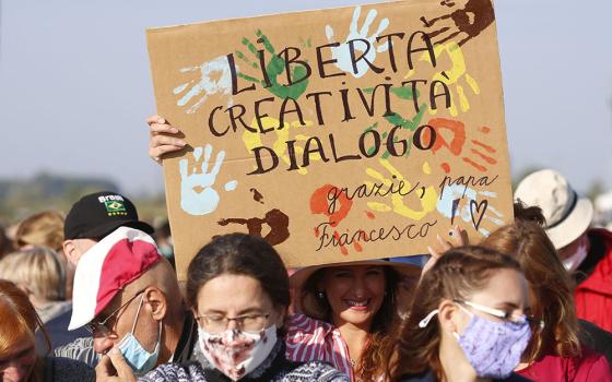 A woman holds a sign in Italian reading "Liberty, Creativity and Dialogue" as people wait for Pope Francis' arrival to celebrate Mass on the fields outside the Basilica of Our Lady of Seven Sorrows in Sastin, Slovakia, Sept. 15. (CNS/Paul Haring)