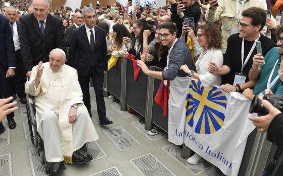 Pope Francis greets a crowd of people while sitting in a wheelchair