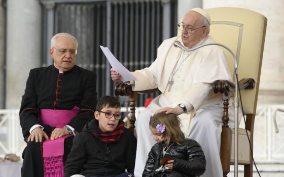 Pope Francis pats the head of a girl after she and another child ran up on to the stage during his weekly general audience in St. Peter's Square Nov. 9, 2022.