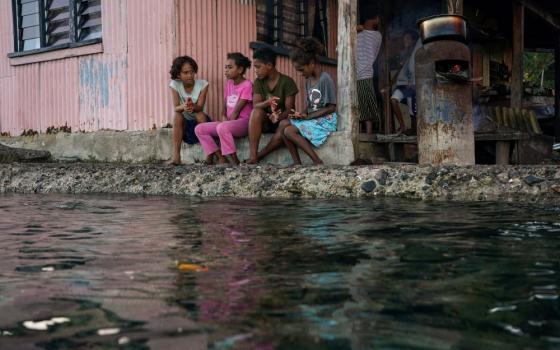 Village children pass the time in front of a home next to a flooding sea wall at high tide in Serua Village, Fiji, July 15, 2022. (CNS/Reuters/Loren Elliott)