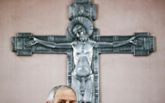 The top half of a man's head is seen below a large metal crucifix on a wall