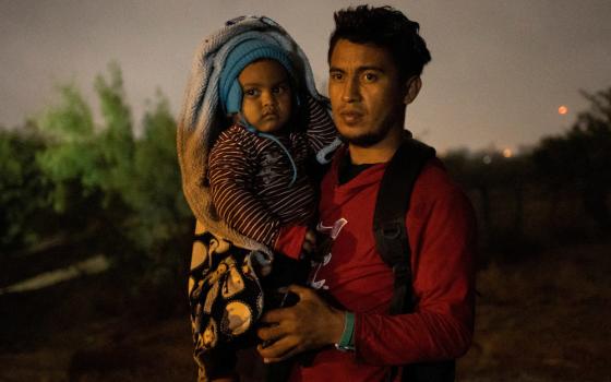 A man holds his small child who is bundled up for the cold night