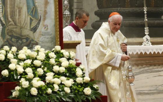 Cardinal Ouellet wears white vestments and stands next to a replicate tilma of Our Lady of Guadalupe