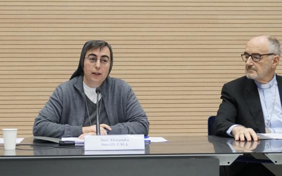 A white sister wearing a grey habit sits next to a white cleric wearing a suit