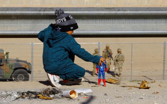 A child wearing a hat and coat plays with a Captain America figure in the desert