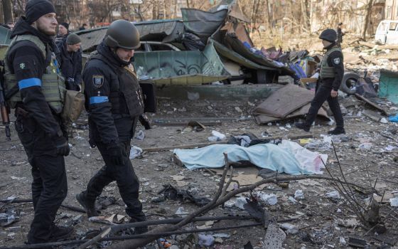 Ukrainian service members stand next to a dead body at a residential district that was damaged by shelling in Kyiv, Ukraine, March 18, 2022, as Russia's invasion of Ukraine continues. (CNS photo/Marko Djurica, Reuters)