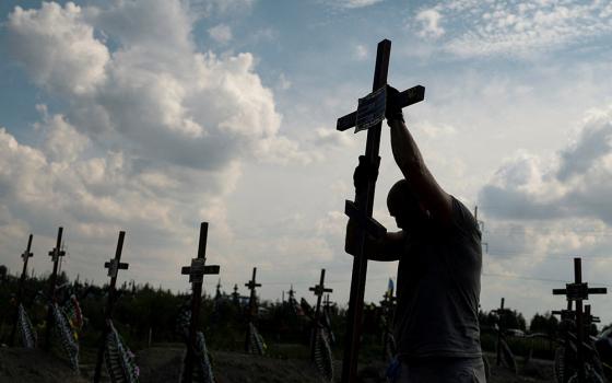 A volunteer places a cross with a number on a grave of an unidentified person during an Aug. 17 mass burial ceremony in Bucha, Ukraine, as Russia's attack on Ukraine continues. (CNS/Reuters/Valentyn Ogirenko)