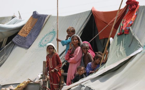 Children displaced by flooding stand outside their family tent while waiting for food handouts and relief material in Sehwan, Pakistan