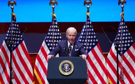 Biden stands behind a podium and in front of four American flags