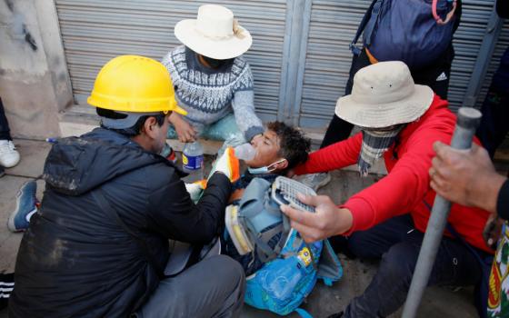 A man wearing a safety helmet holds a breathing device over another man who lays on the ground