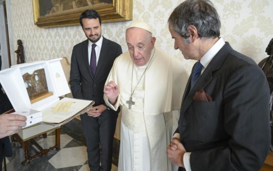 Pope Francis closes his fingertips in a hand gesture as he speaks to an older white man in a suit