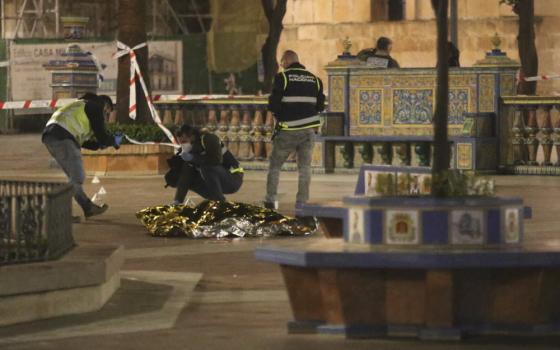 Police kneel and stand around a gold emergency blanket in the middle of a colorful plaza