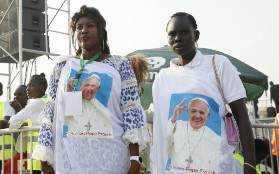 Two Black women wear wraps around their clothes with Pope Francis' face printed on them