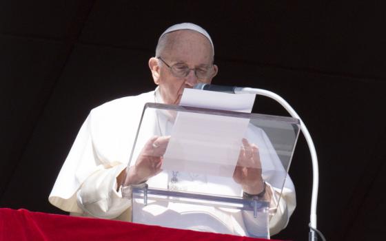 Pope Francis speaks into a microphone while holding a piece of paper over a clear lecturn