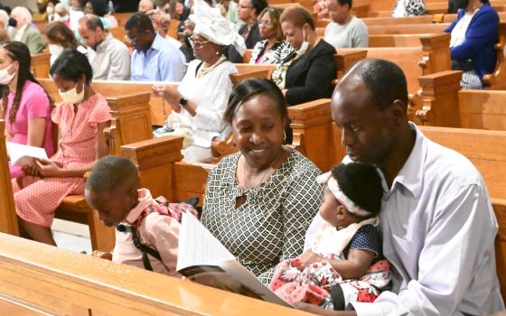 A Black family with two small children sits in a pew surrounded by other Black Catholics