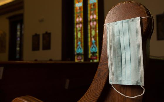 In this illustration photo, a disposable medical mask hangs on the side of a pew. (CNS/The Catholic Spirit/Dave Hrbacek)