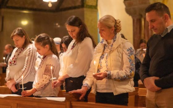 Five people, some wearing brightly embroidered sweaters and shirts, hold candles