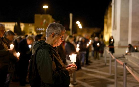 An older white man holds a candle while standing outside in a crowd at night