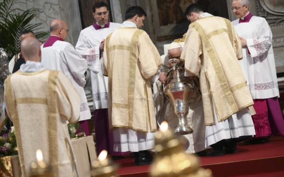 Pope Francis bends over a silver urn, while surrounded by men in white and golden vestments