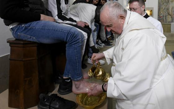 Pope Francis, without his zuchetto, pours water over a person's foot, who can be seen from the waist down wearing jeans