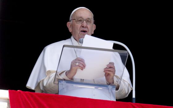 Pope Francis reads from a sheet of paper, while standing behind a microphone and a clear lecturn