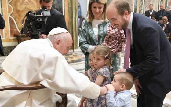 A toddler holds Pope Francis' hand as his sisters and parents stand around him