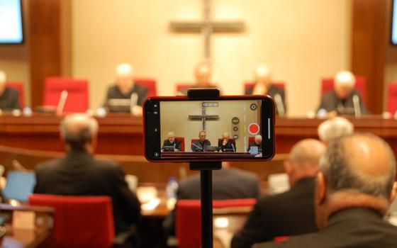 A phone captures video of a press conference led by several clerics in front of a crucifix