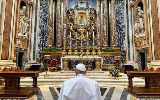 Pope Francis is shown from the back as he prays to icon of Mary.