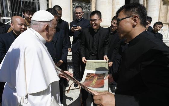 Pope Francis talks to a group of Chinese men wearing clergy collars and black suits. The men hold a unfurled scroll with artwork.