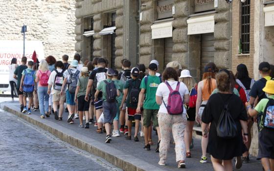 A large group of people wearing walking clothing move along a sidewalk at the side of a stone street