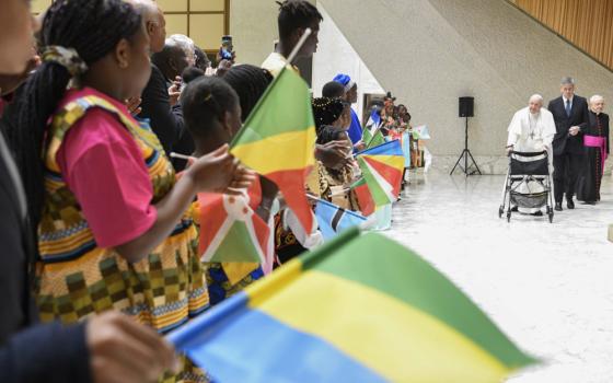 Pope Francis uses a walker to walk towards a long line of African children holding various colorful flags