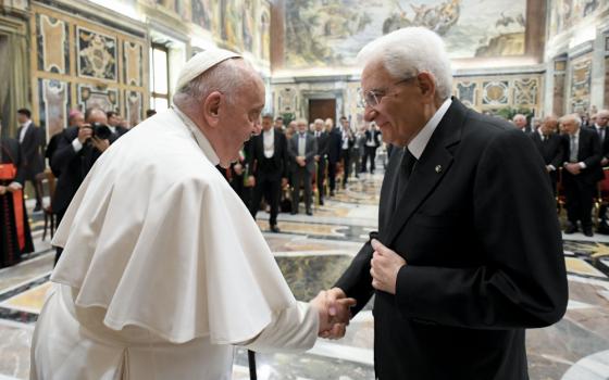 Pope Francis, using his cane, shakes the hand of an older white man wearing glasses