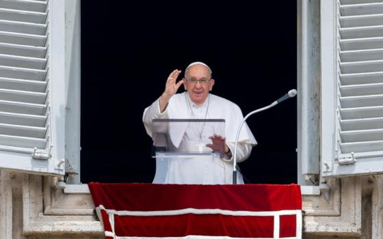 Pope Francis smiles and waves as he stands in the open window of his apartment