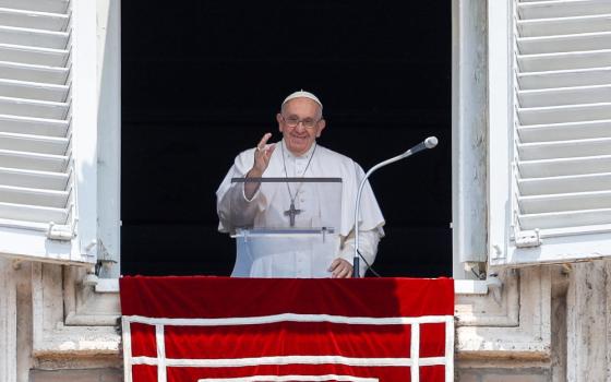 Pope Francis raises his hand as he stands in the window of his Vatican apartment