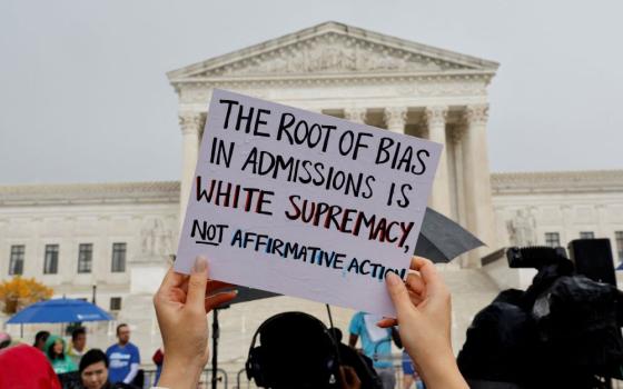 Demonstrator holds sign outside Supreme Court. It reads, "The root of bias in admissions is white supremacy, not affirmative action."